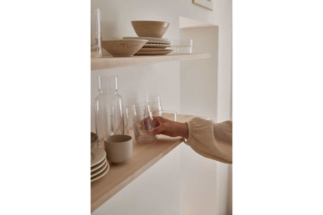 a woman puts a stack of glassware together in a minimalist scandi setting